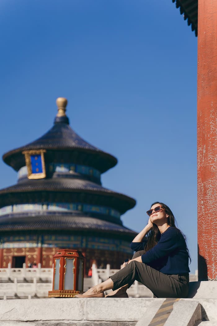 mujer con gafas sentada frente a un templo chino en beijing.