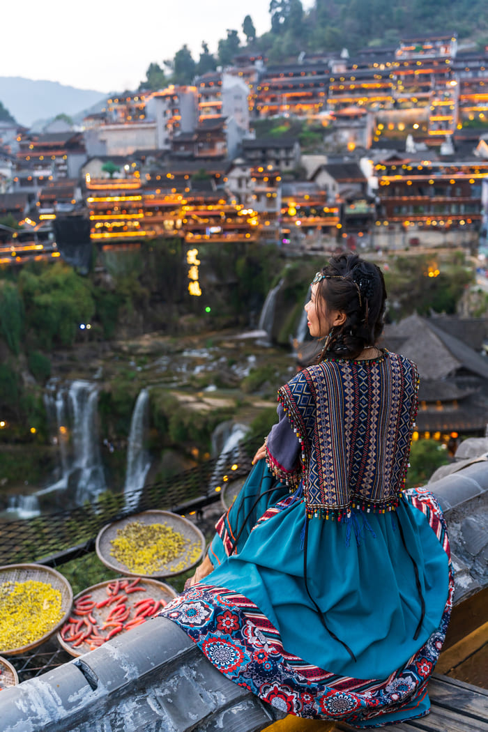 mujer sentada mirando hacia las luces la ciudad de lijiang.